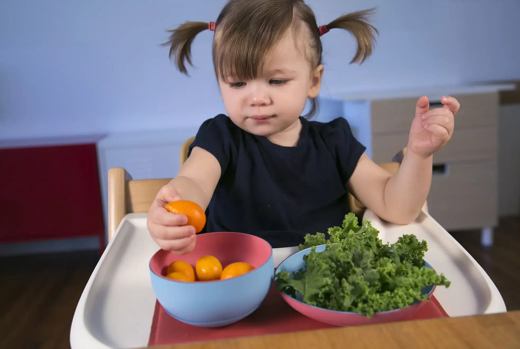 A baby playing with a tangerine above the Bumble magnetic flatware set.
