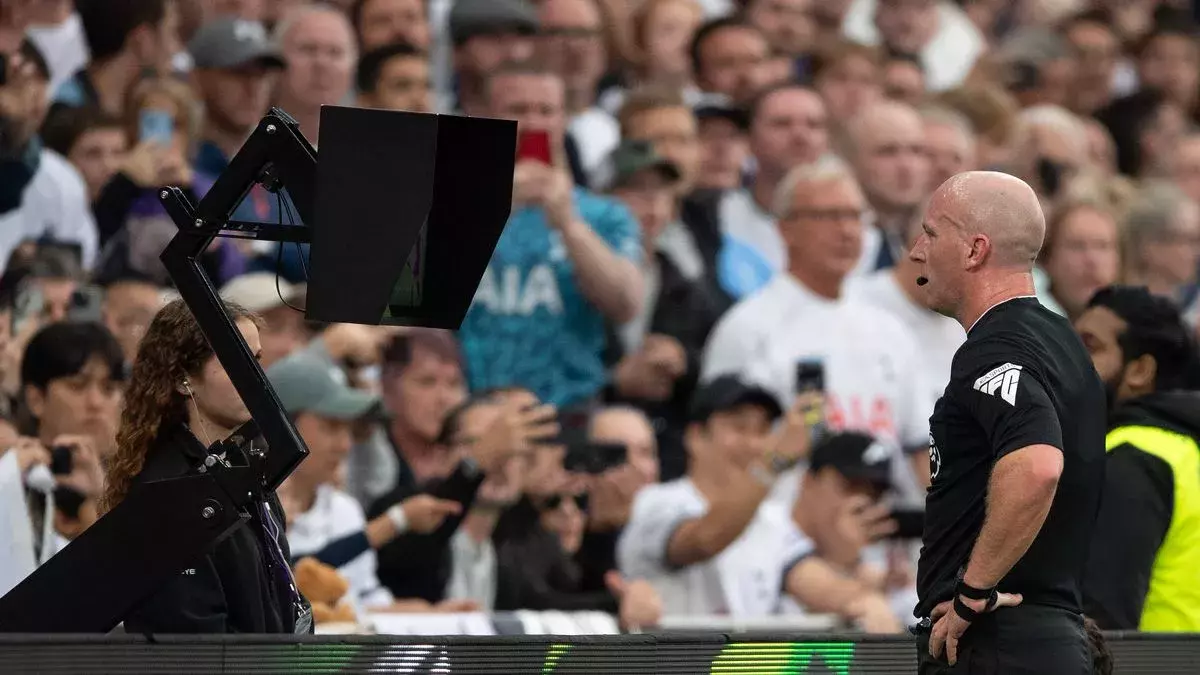 A premier league referee looking at a monitor as the VAR assistants are talking in his ear explaining a play.